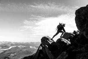 Black and white photo of a man scrambling up a mountain ridge while doing high altitude training.