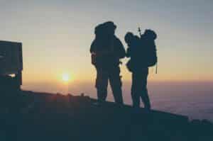 Two people on the summit of a high altitude mountain at sunrise with big backpacks and equipment.
