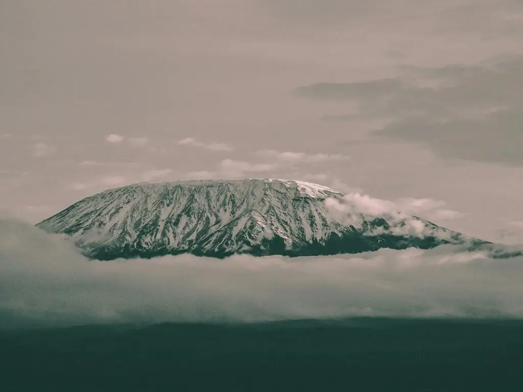 View of Mt Kilimanjaro with a snow-covered summit and clouds just underneath.