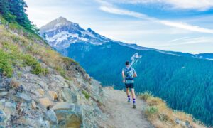 A man running on a trail in the mountains with a peak in the distance.