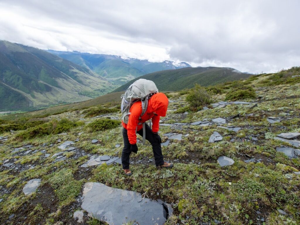 A man hunched over trying to catch his breath wearing a backpack on a mountain.