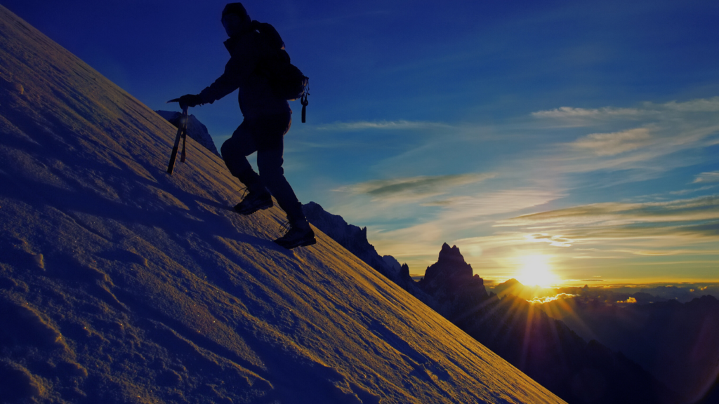 A trekker climbing a snowy mountain with a stunning sunset sky in the background.